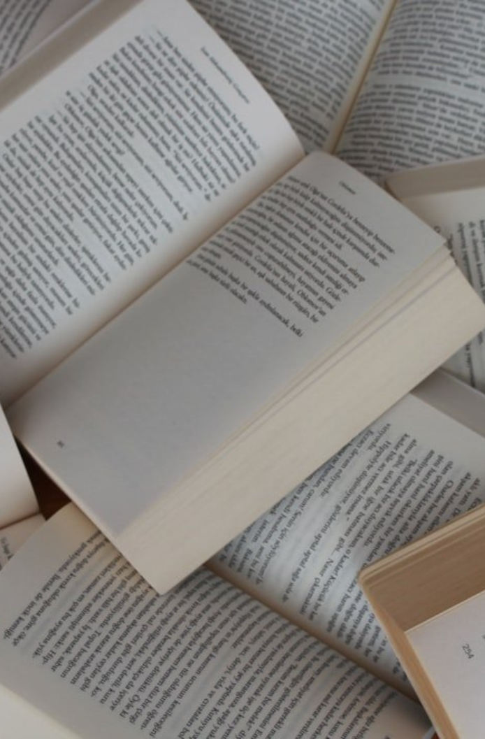 A scattered arrangement of open books with visible text on their pages.